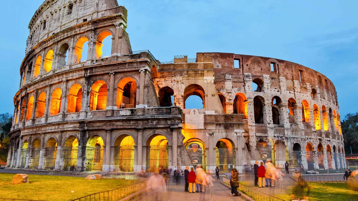 The Colosseum lit from within during an evening guided tour, arches glowing against a dark blue sky in Rome